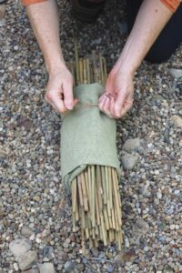 person tying twine around bamboo stakes wrapped in burlap